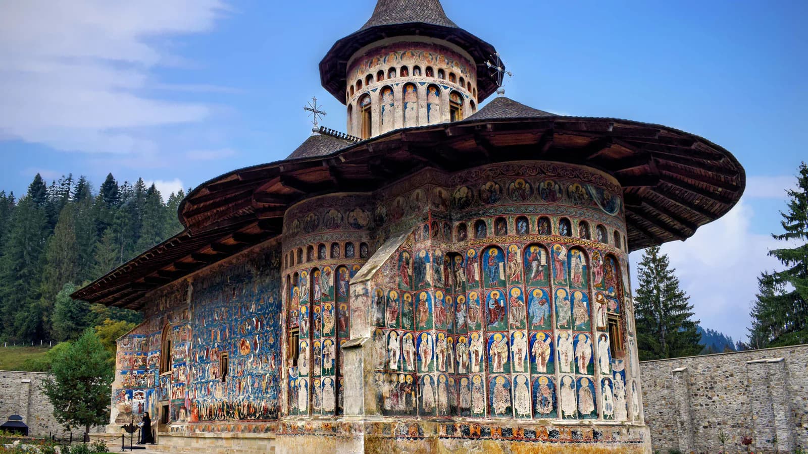 Biserica Mănăstirii Voroneț, cu frescele exterioare și dealurile împădurite ale Bucovinei